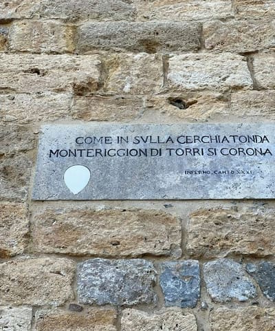la lapide murata nella cinta con i versi dell'Inferno, "come in sulla cerchia tonda Monteriggion di torri si corona"