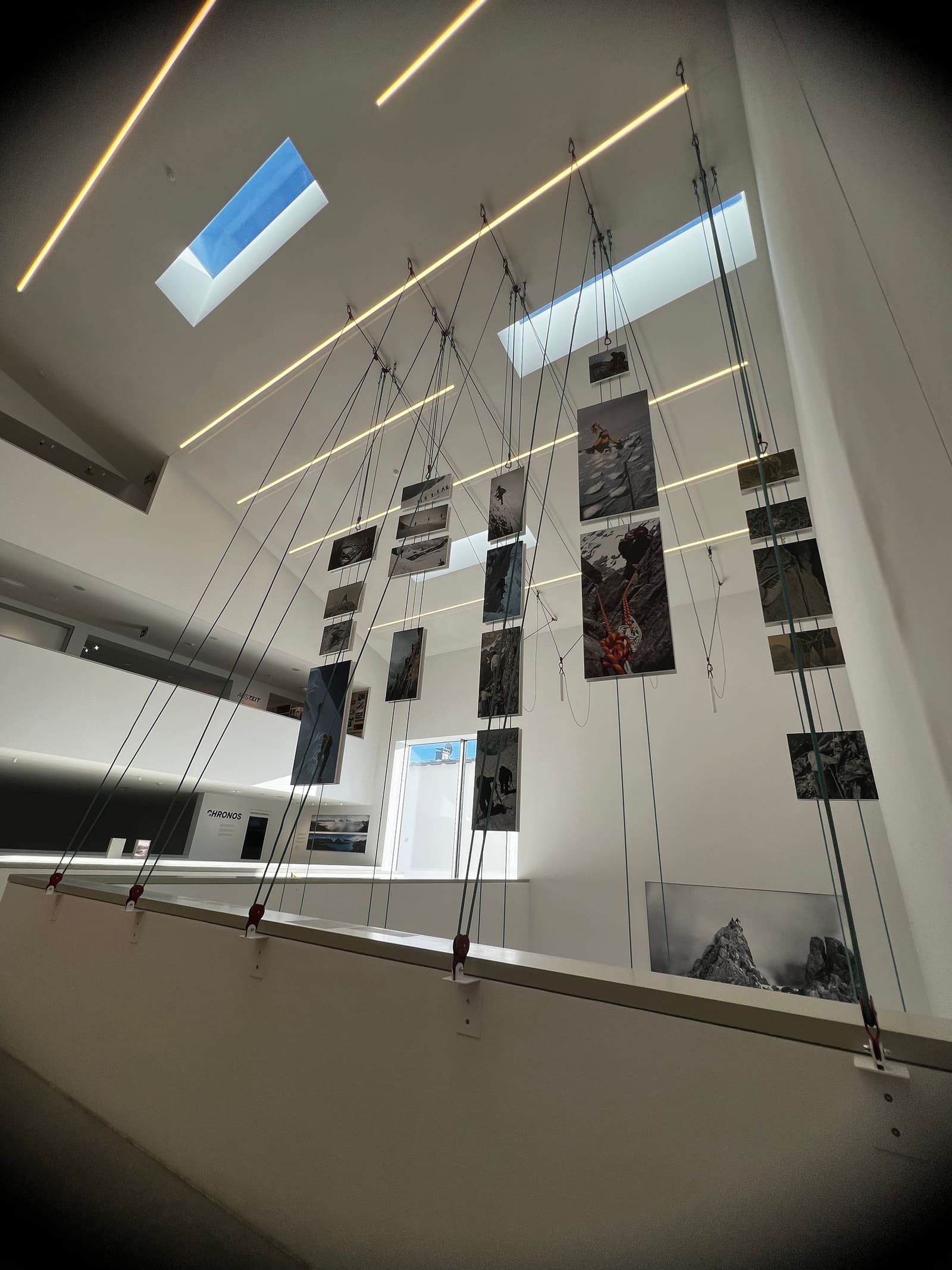 le fotografie appese ai cavi d'acciaio, nel vuoto della sala