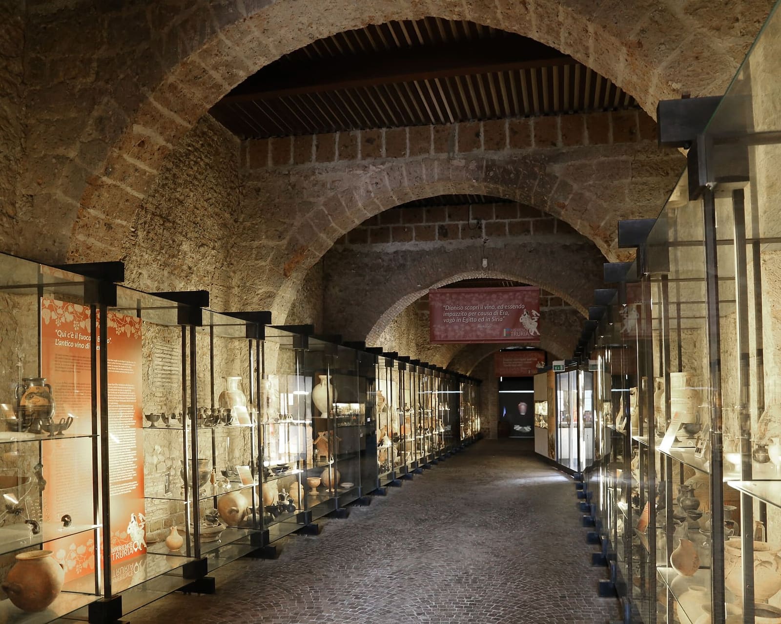 la galleria del museo cerite sotto le arcate di pietra, con le vetrine dei vasi in fila da una parte e dall'altra