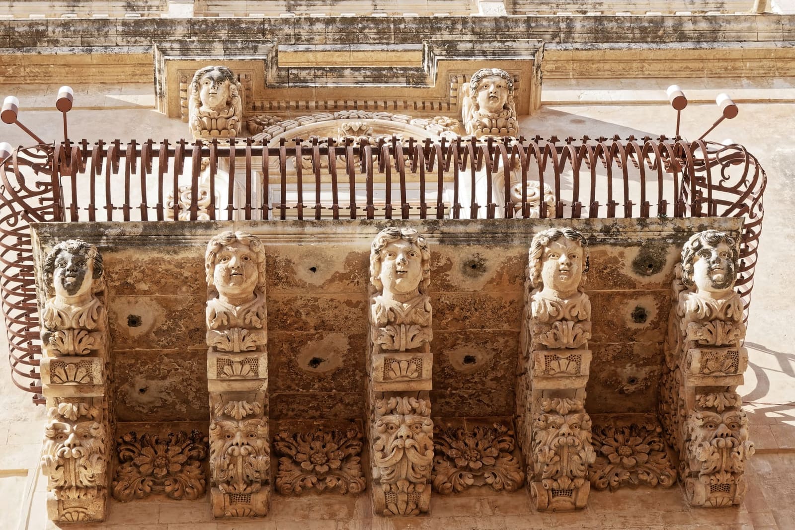 un balcone di Palazzo Nicolaci visto da sotto, con i mensoloni scolpiti a volti e figure