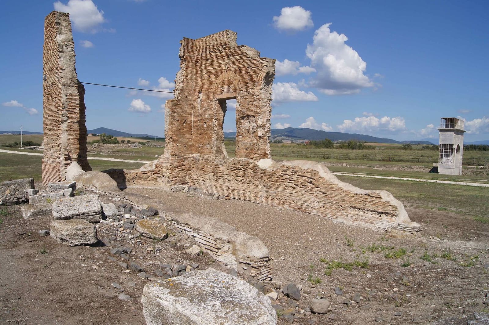 i muri di mattoni della basilica romana, con la finestra ancora in piedi sotto l'arco di scarico, e in fondo a destra l'arco onorario sul decumano