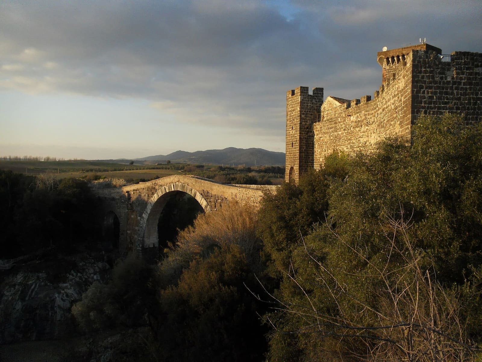 il castello e il ponte al tramonto, con la luce bassa sulle mura merlate e la campagna che si spegne in fondo