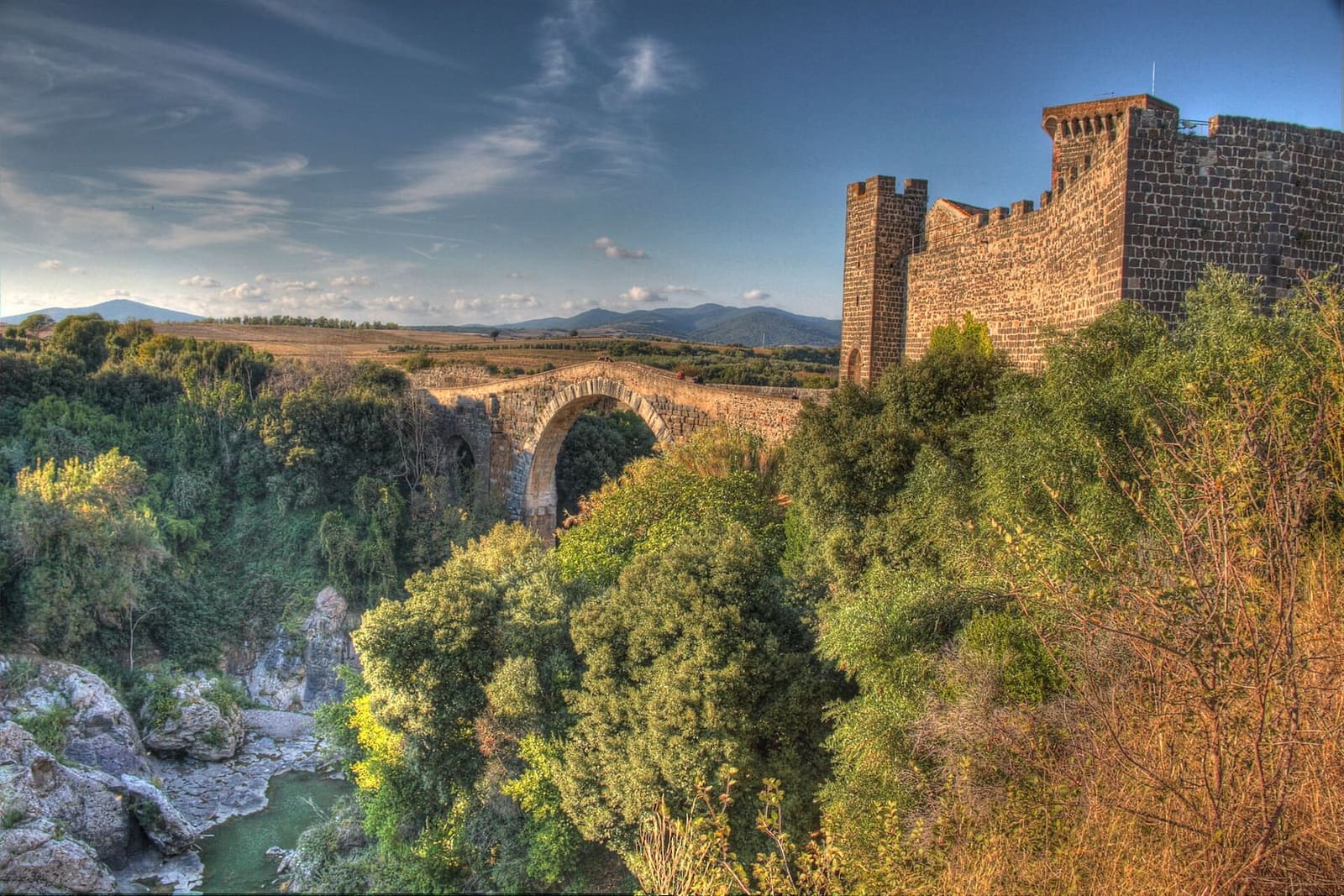 il castello e il ponte dall'alto, con la gola piena di verde sotto le mura merlate e la campagna che corre fino ai monti