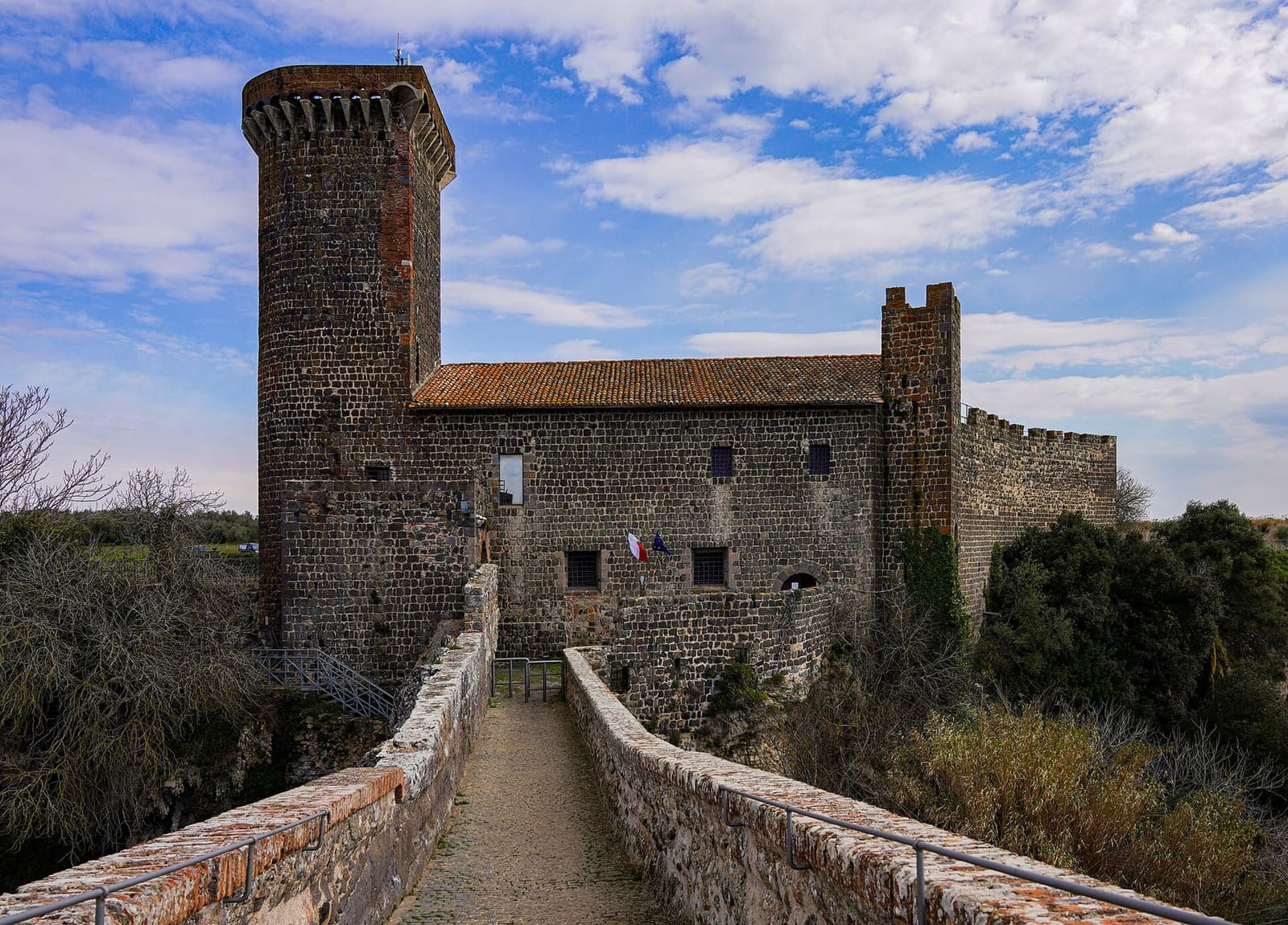 il castello dell'Abbadia visto dal ponte, con la torre tonda, il palazzo con il tetto di coppi e il passaggio stretto fra i parapetti
