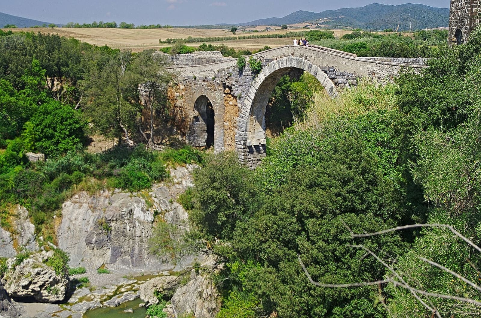 il ponte dell'Abbadia sopra la gola, con le rocce chiare del Fiora sotto, il verde fitto sulle pareti e la torre del castello che spunta a destra