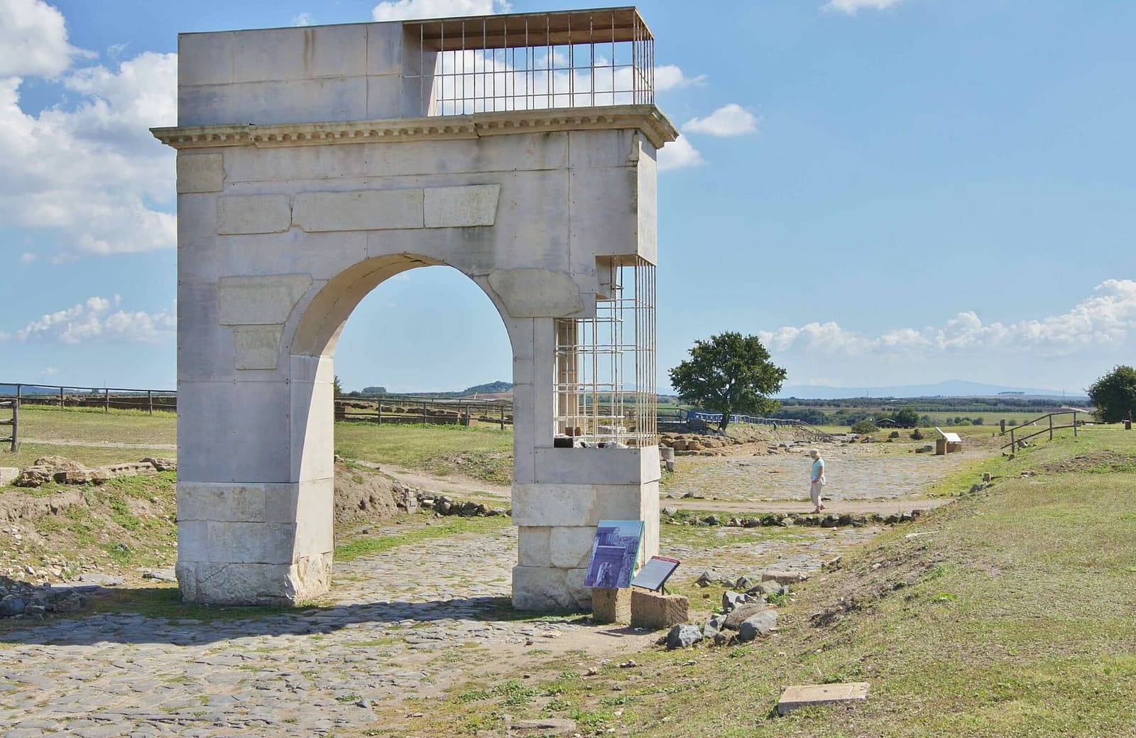 l'arco onorario di Publio Sulpicio Mundo rimesso in piedi sul decumano, con le parti nuove in pietra chiara e la gabbia di metallo dove mancano i blocchi, e il basolato che prosegue verso la campagna