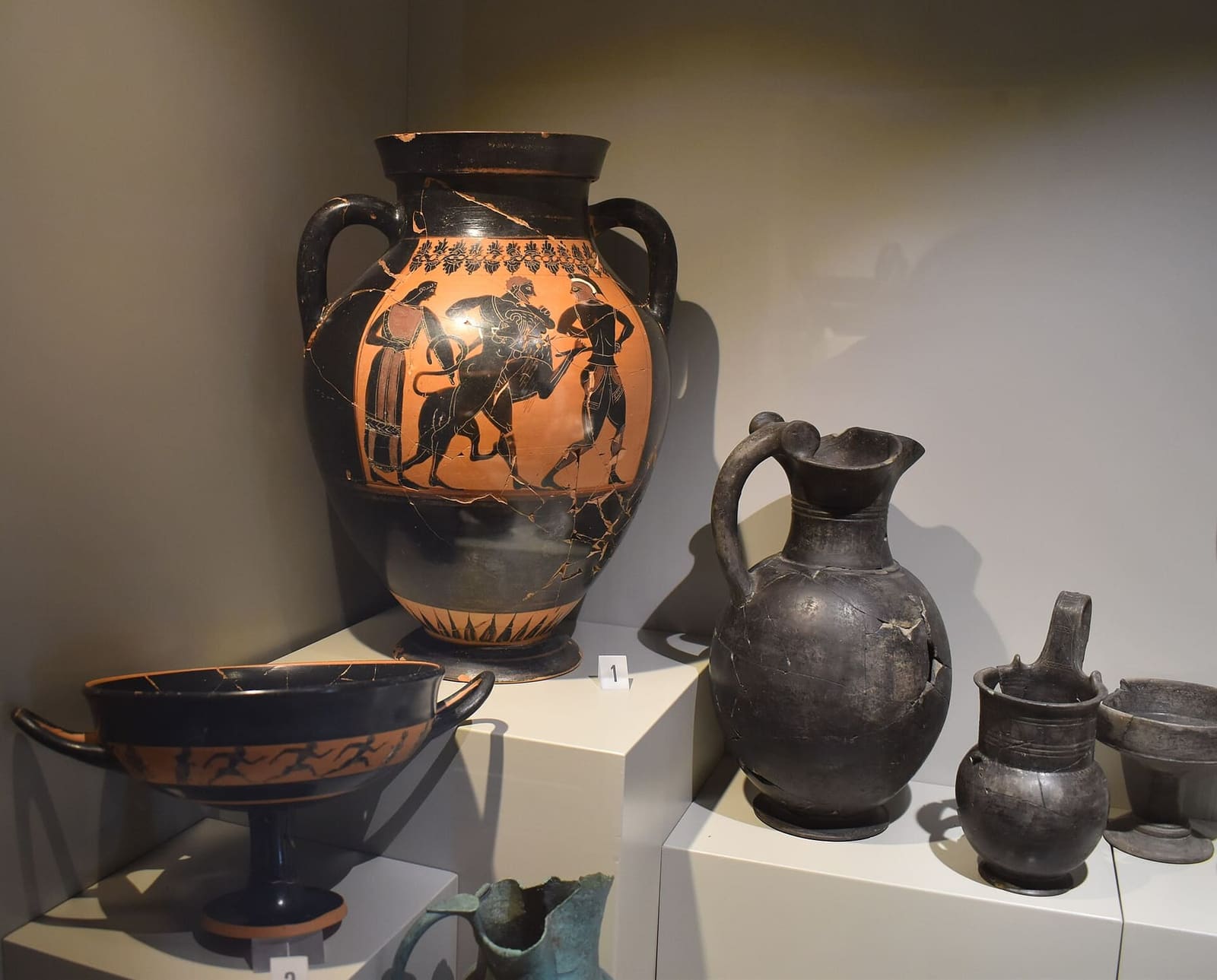 una vetrina del museo con un'anfora a figure nere, una coppa e i vasi di bucchero nero lucido