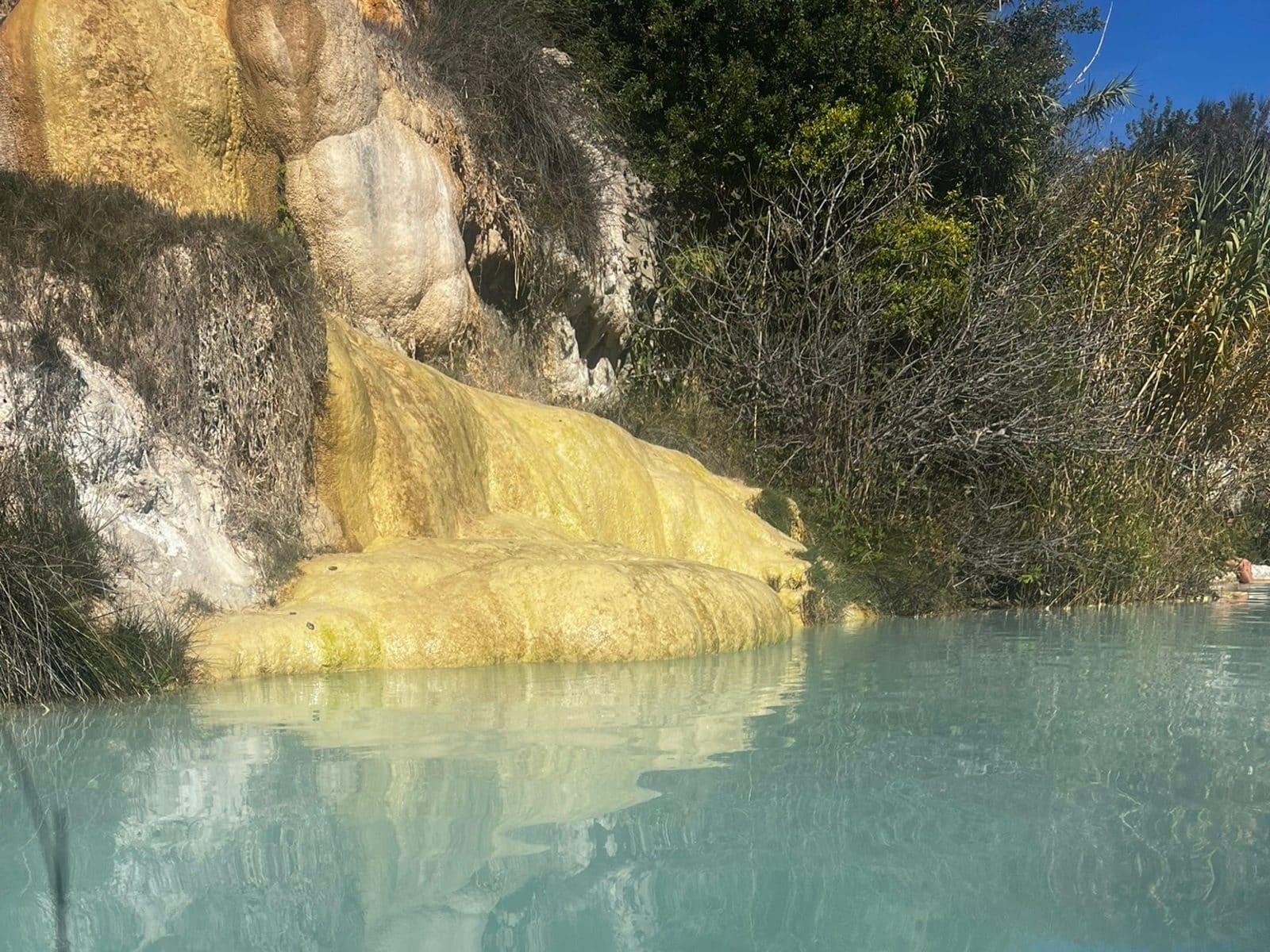 la colata di travertino giallo depositata dall'acqua calda, che scivola dentro la pozza fra la macchia
