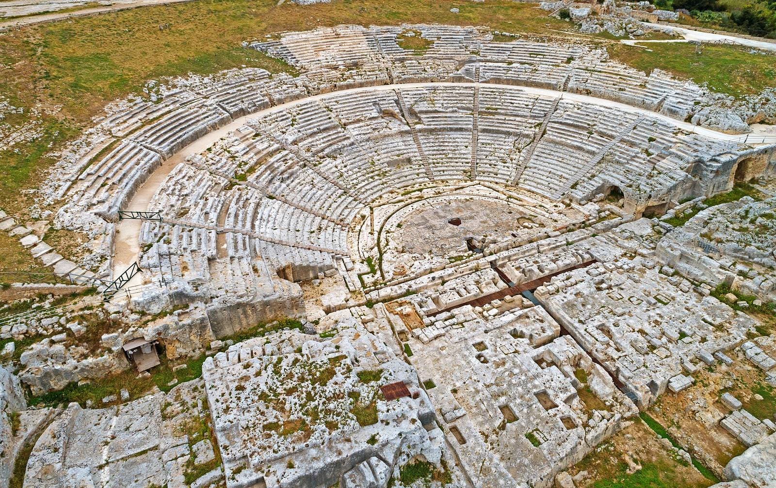 das Griechische Theater von oben, mit den in den Fels gehauenen Sitzreihen und den Einschnitten des Bühnengebäudes vor der Orchestra
