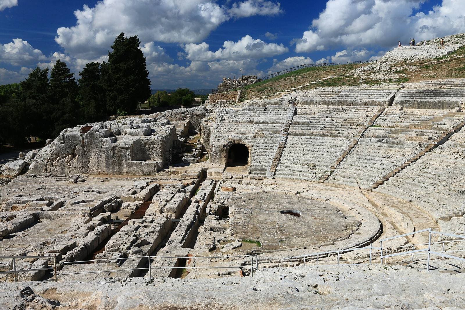 le gradinate del Teatro greco intorno all'orchestra, con l'apertura della grotta del Ninfeo in alto