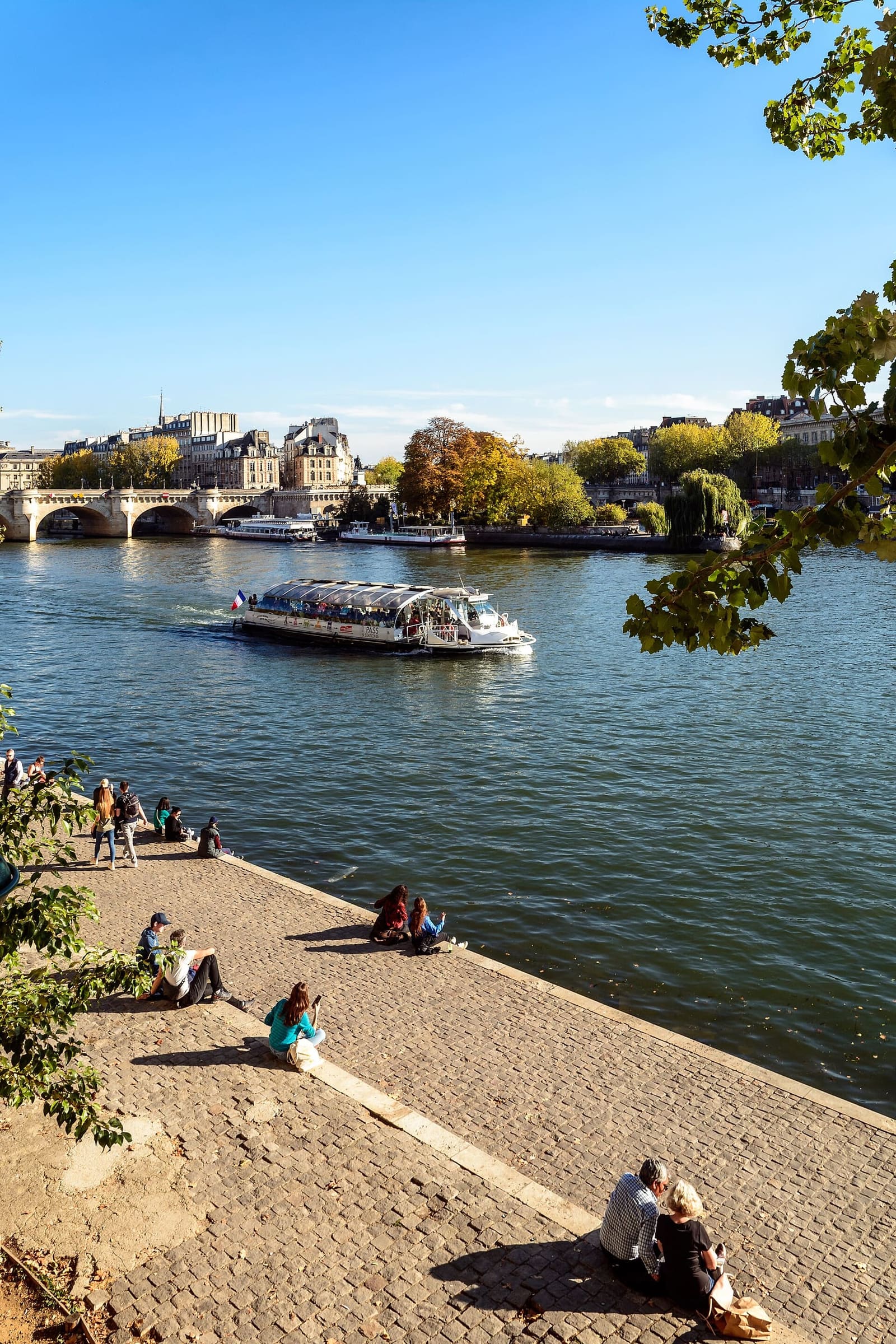 people sitting on the quay along the Seine, with a boat and the Île de la Cité in the distance