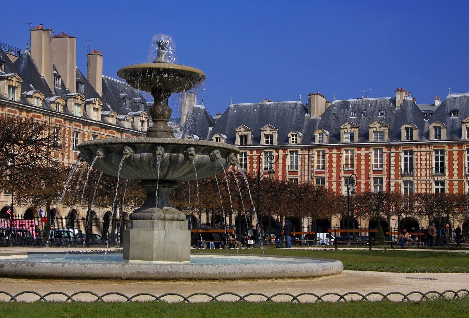 a fountain on Place des Vosges in front of the brick and stone pavilions
