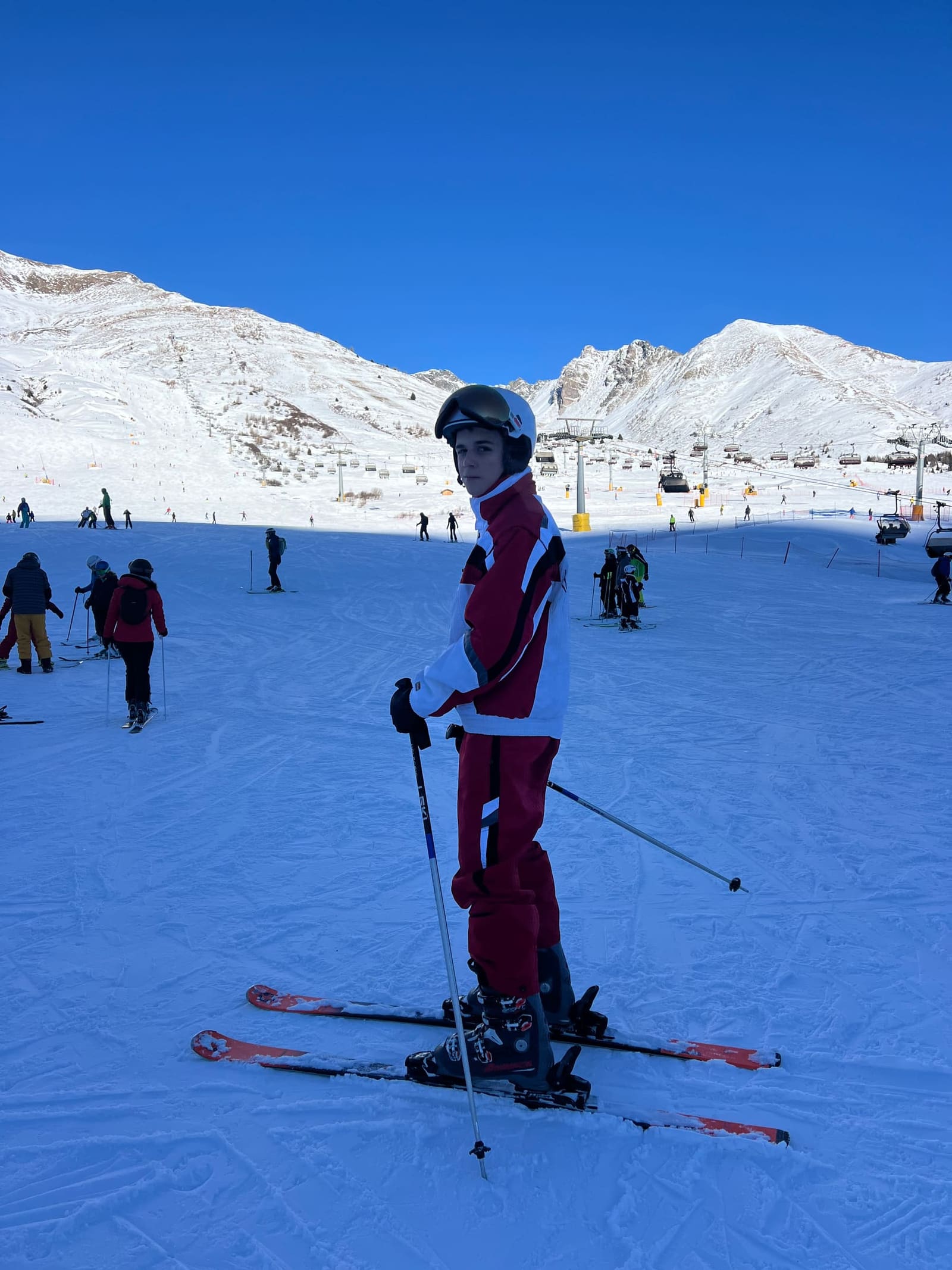 nostro figlio in piedi sugli sci in mezzo alla pista, con le seggiovie dietro