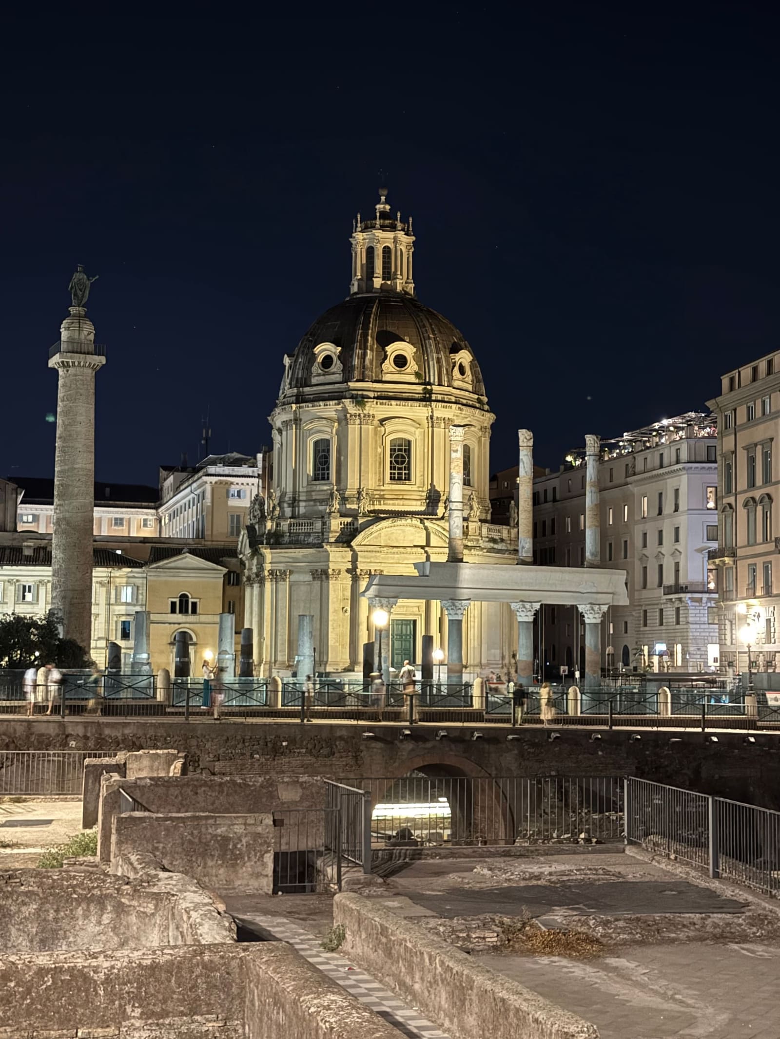 la Colonna Traiana da vicino, con i rilievi della guerra dacica che si avvitano per trenta metri e la chiesa illuminata a fianco