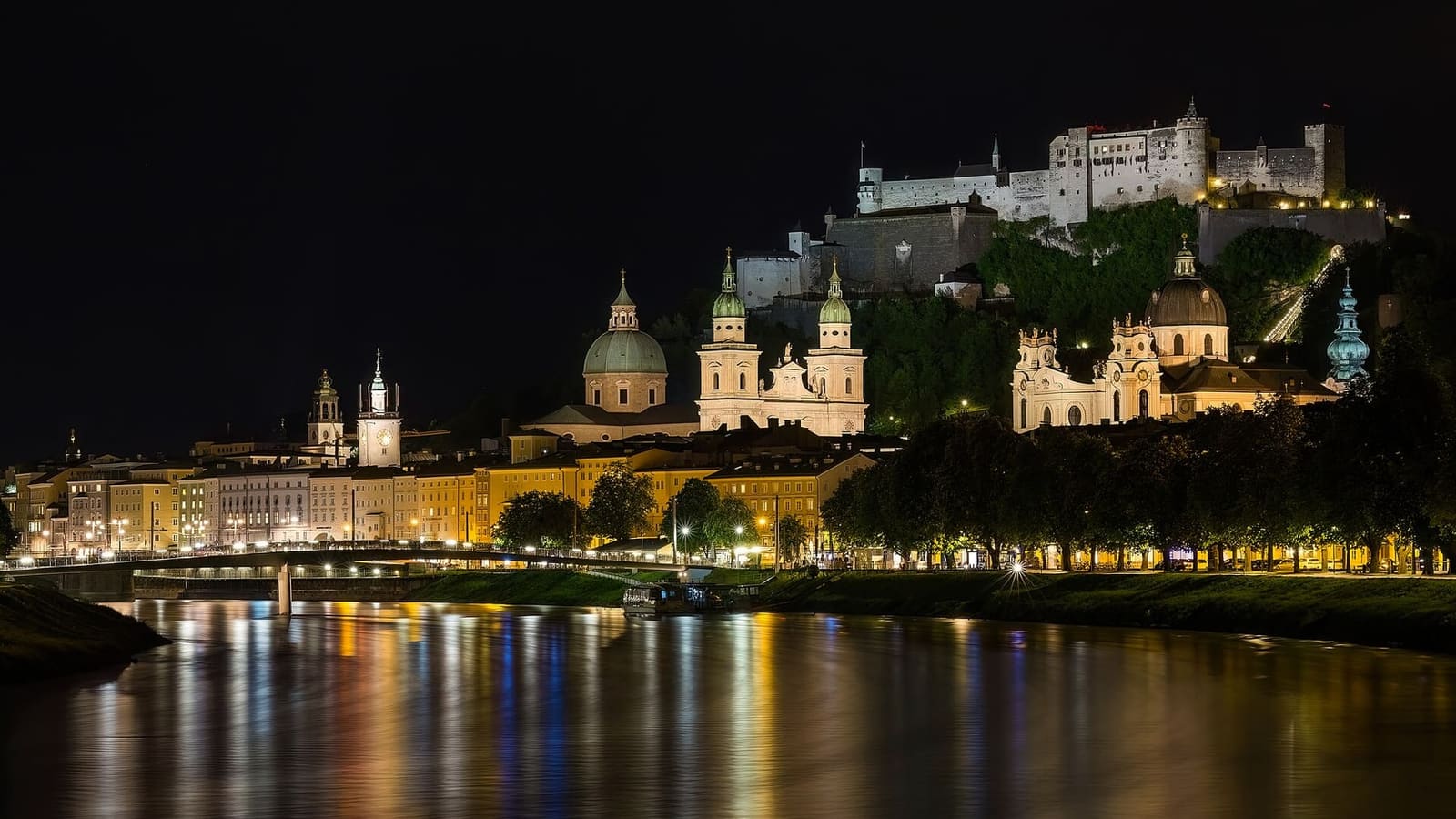 la città vecchia di sera dalla riva del Salzach, con il duomo, la Kollegienkirche e la fortezza illuminati