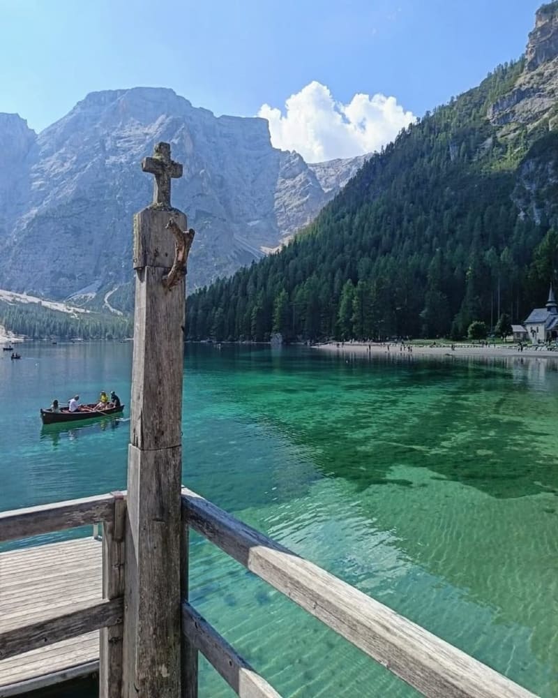 il Lago di Braies dal pontile di legno, la croce in primo piano e una barca sull'acqua verde