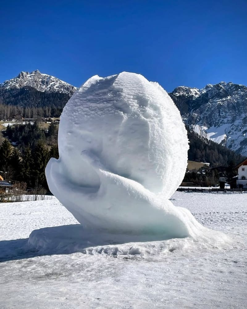 una grande scultura di neve nel prato del paese, con le cime dietro