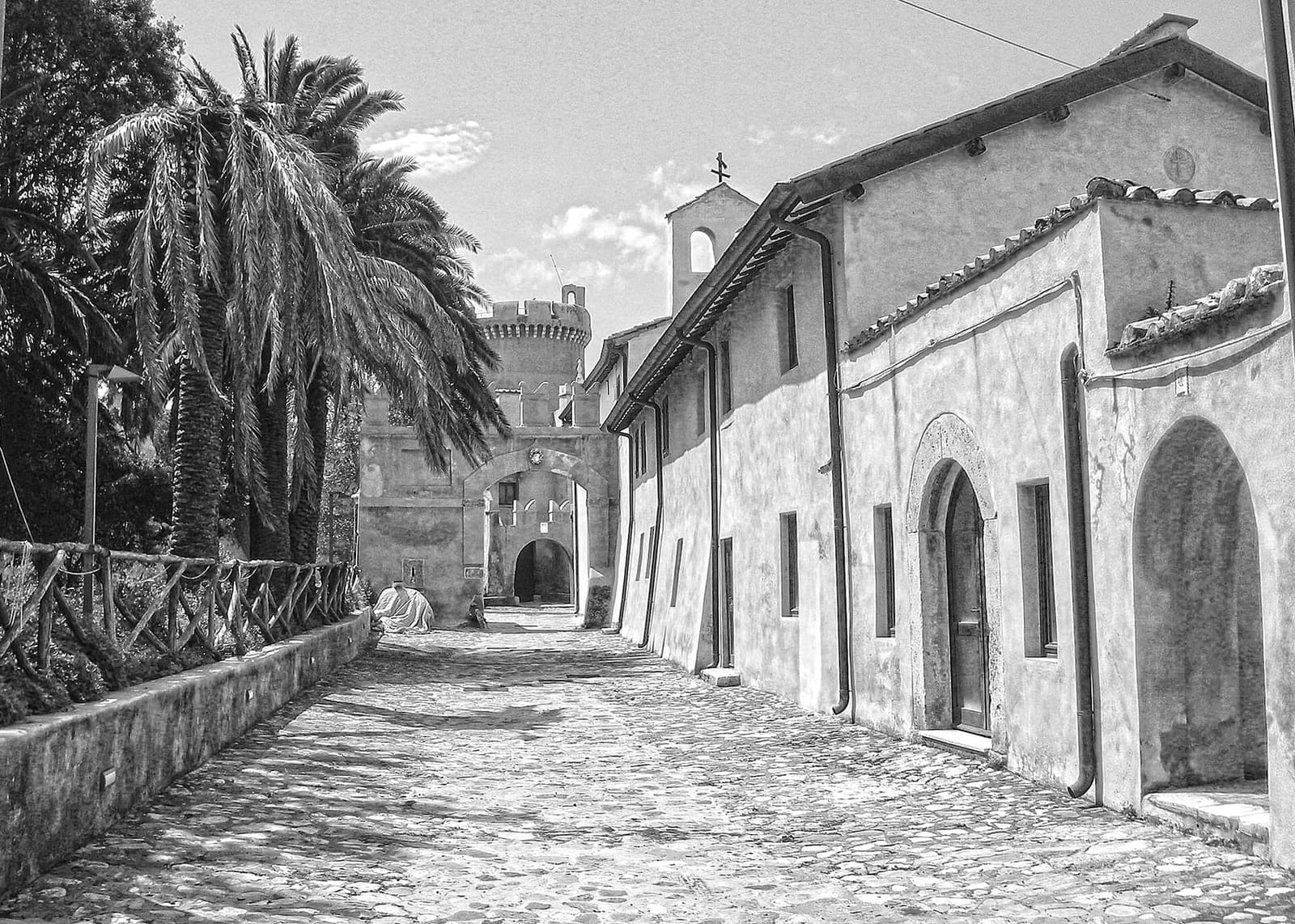 la strada acciottolata del borghetto dentro le mura, con le palme a sinistra, le case basse a destra e in fondo una porta e una torre rotonda