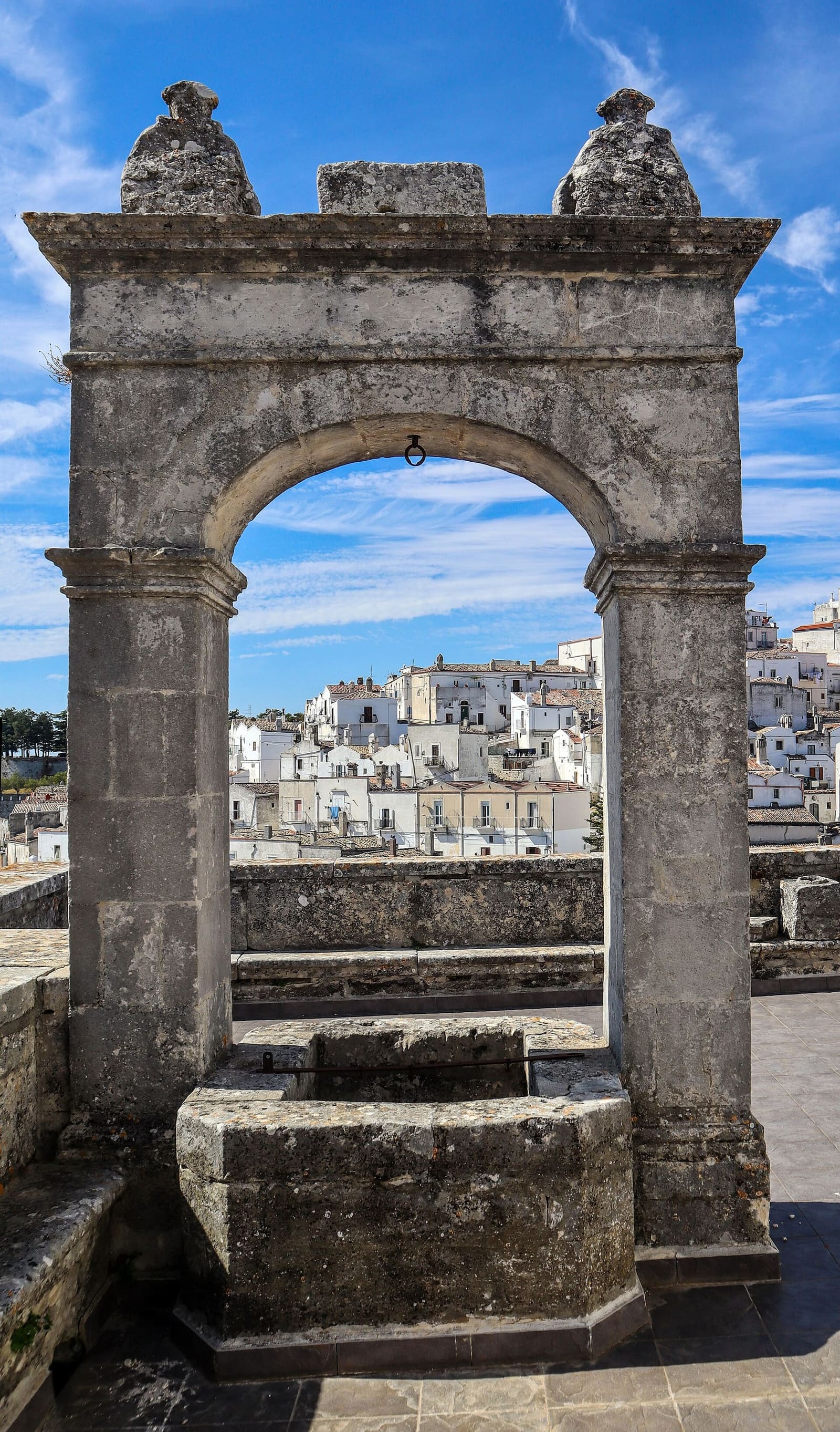 un arc de pierre avec le puits, qui donne sur les maisons du Junno