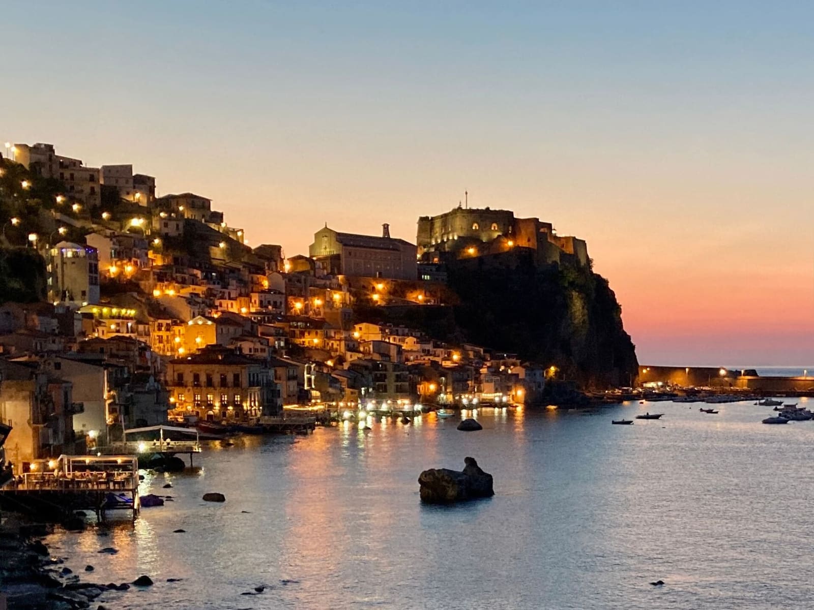 Chianalea illuminata al tramonto, con la rupe del castello