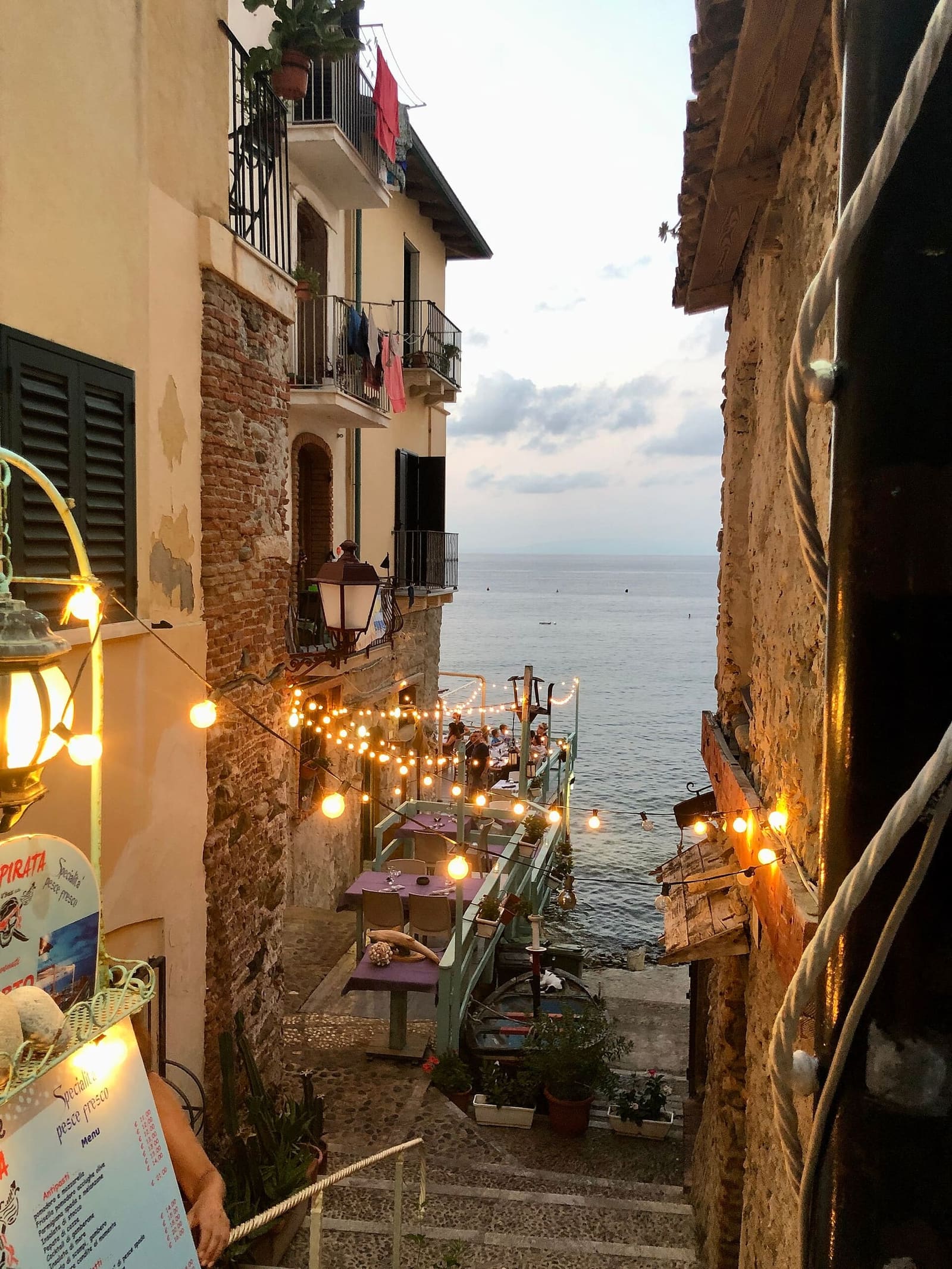 un vicolo di Chianalea la sera, con le luci accese e il mare in fondo