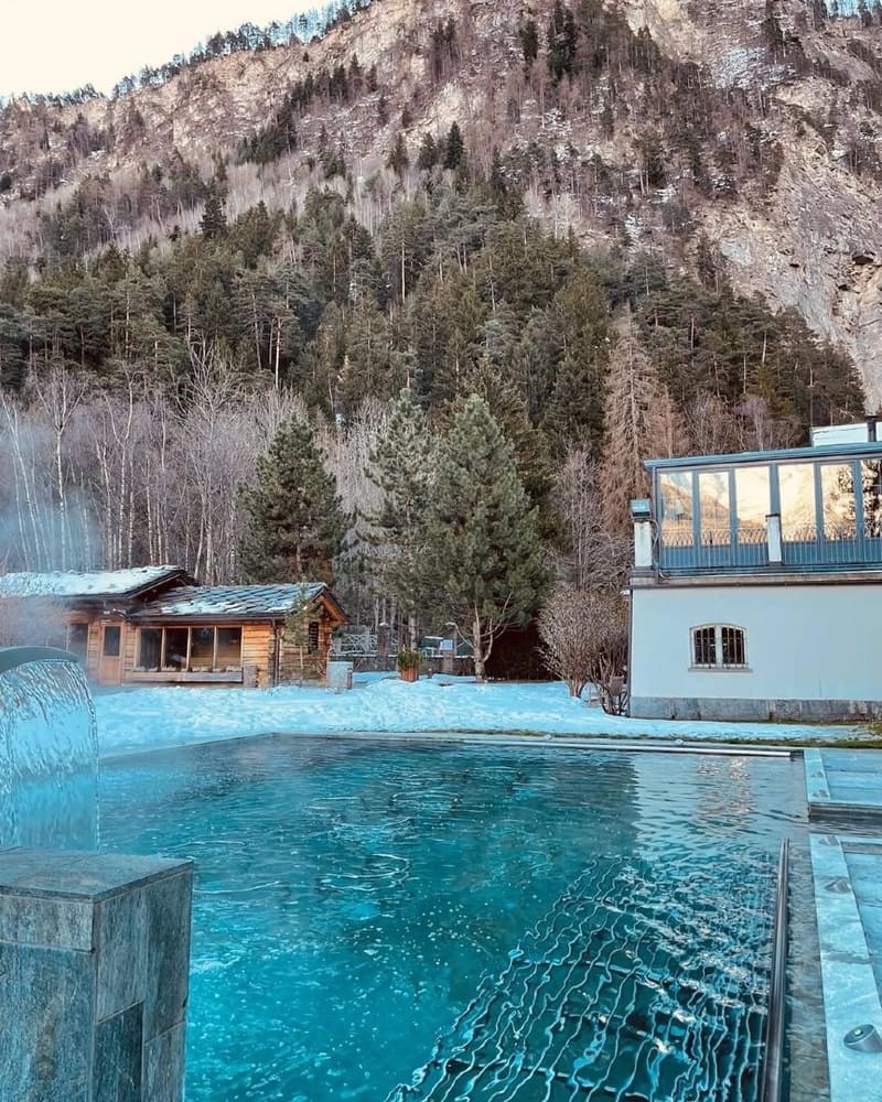 la vasca scoperta con la neve tutt'intorno e la cascata a caduta, la Sauna Chalet sullo sfondo