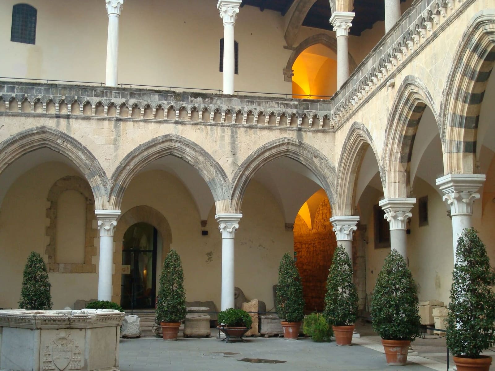 il cortile di palazzo Vitelleschi, i due ordini di logge ad archi, il pozzo e le piante in vaso fra i reperti di pietra