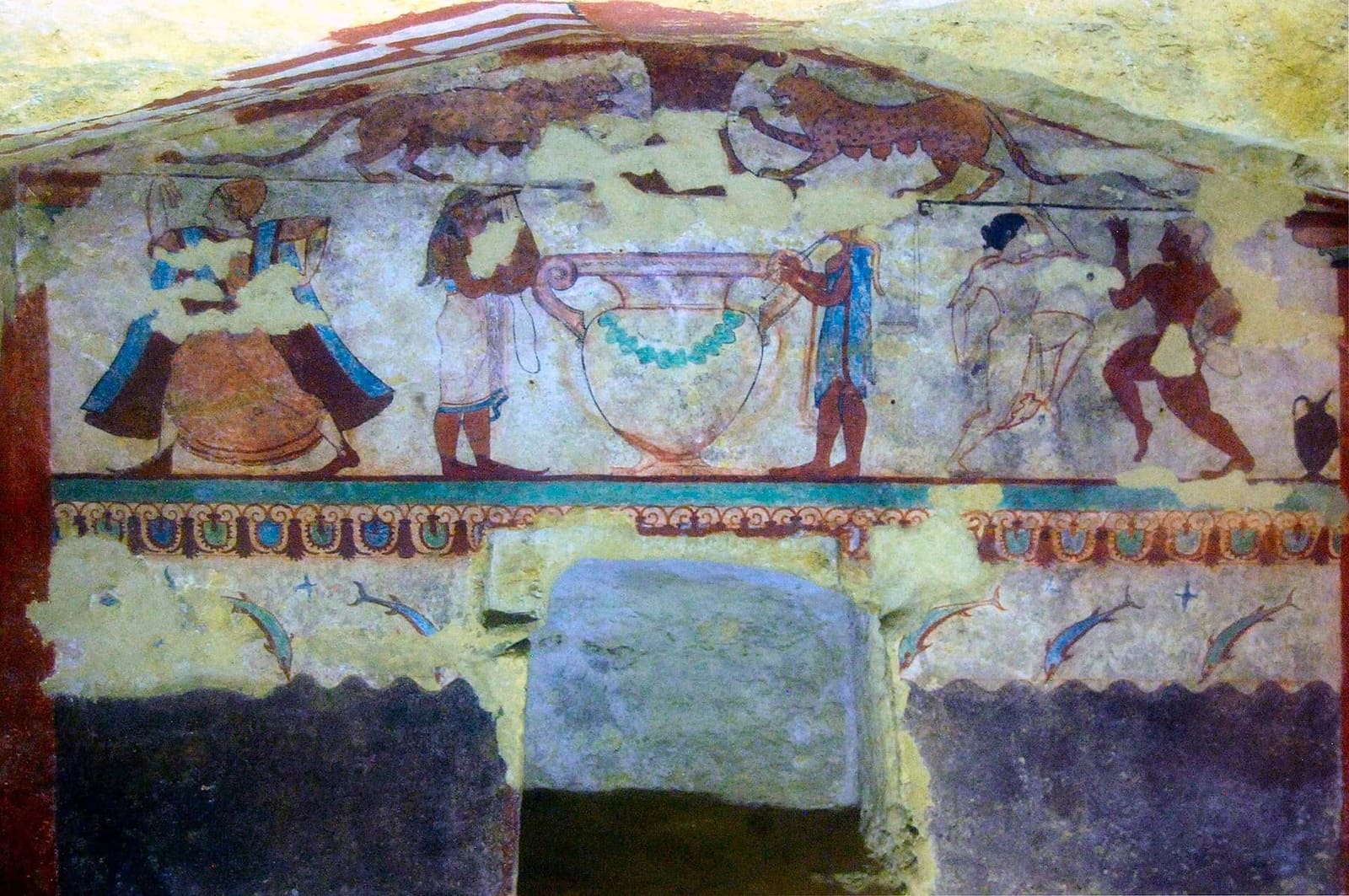 la Tomba delle Leonesse: due felini nel timpano, sotto una danzatrice, il grande cratere con la ghirlanda fra due suonatori e un danzatore, e più in basso i delfini sopra le onde scure