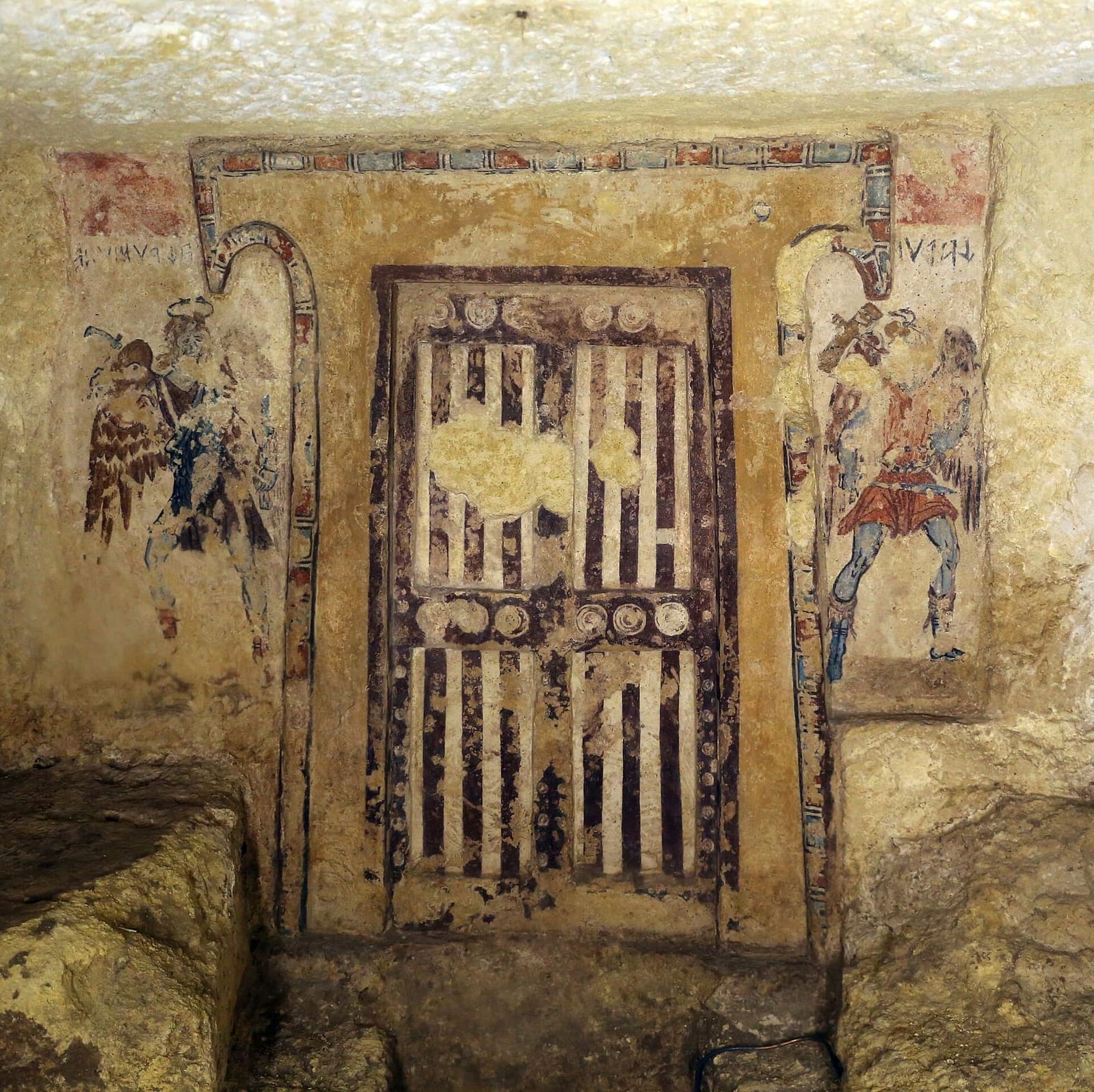 la Tomba dei Caronti: una porta dipinta a borchie e listelli, e ai due lati i demoni alati con il martello che la custodiscono, con i nomi scritti in etrusco