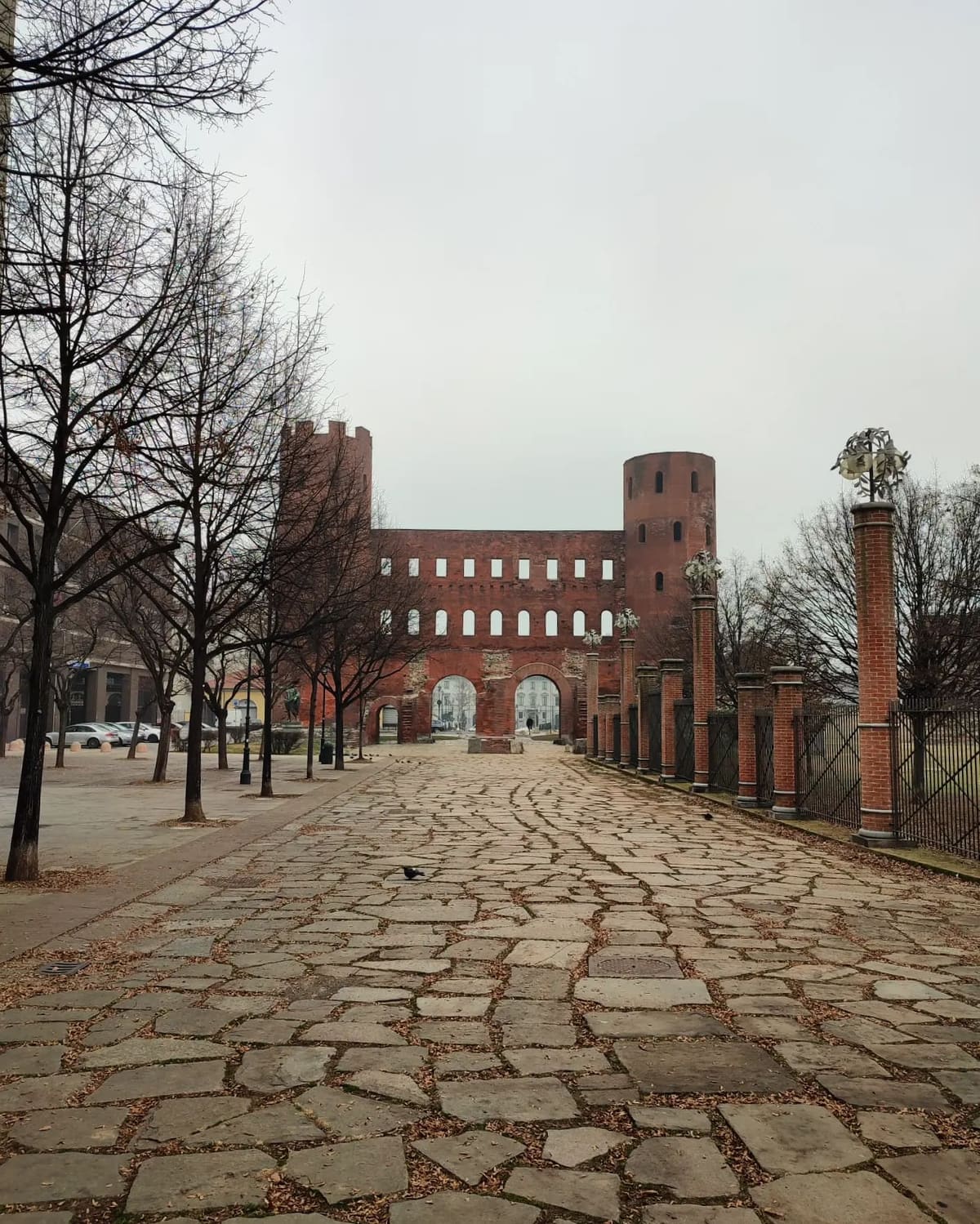 la Porta Palatina con le due torri romane, in fondo al selciato fra gli alberi spogli