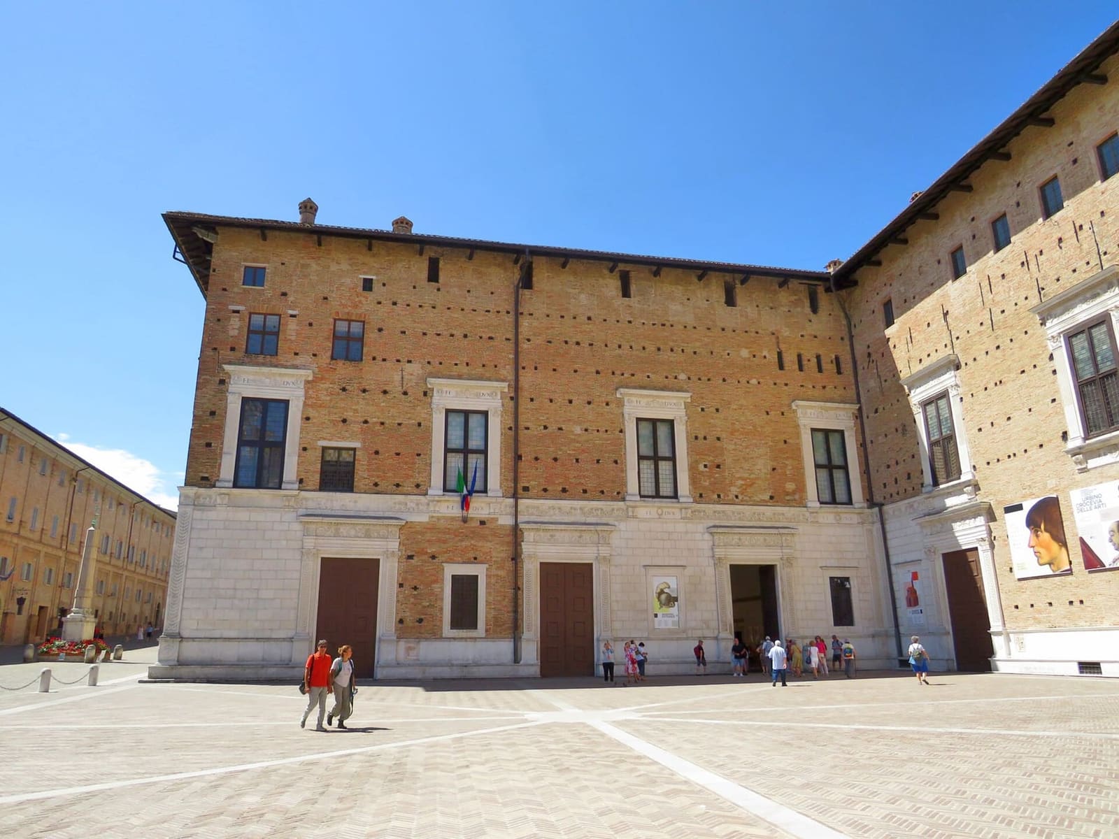 la facciata del palazzo su piazza Duca Federico, con le porte e le finestre incorniciate di pietra bianca che ripetono FE DVX