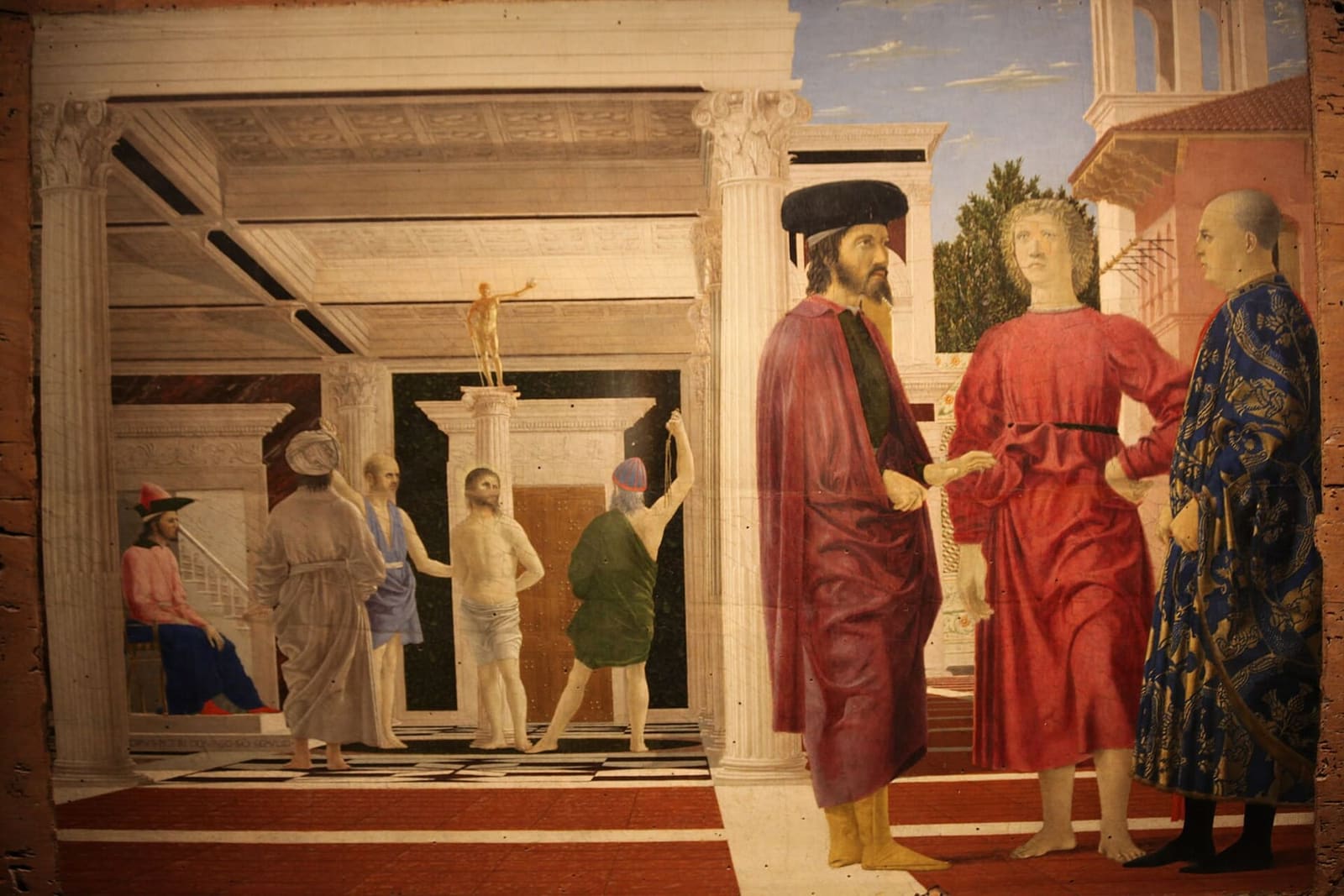 la Flagellazione di Piero della Francesca, con il Cristo legato alla colonna sotto il portico e i tre uomini in primo piano a destra