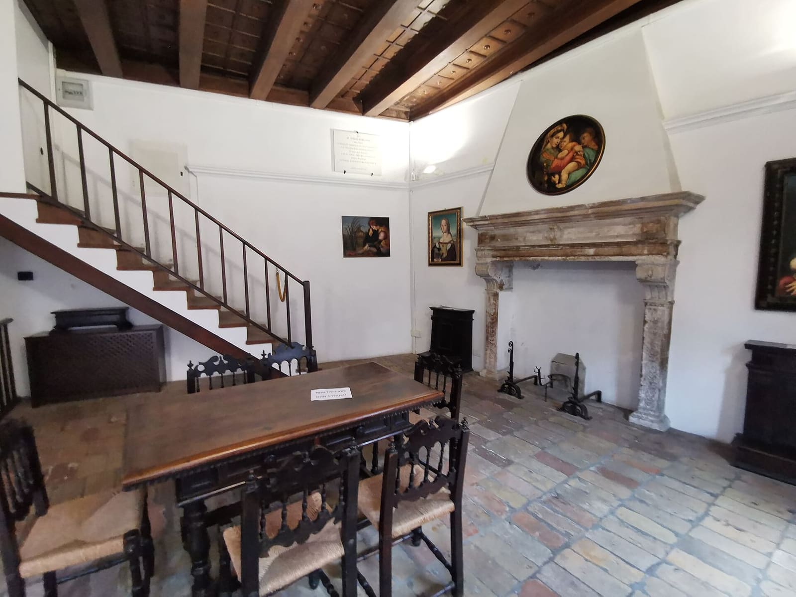 una stanza della casa di Raffaello, con il camino di pietra, il soffitto di travi e la scala di legno