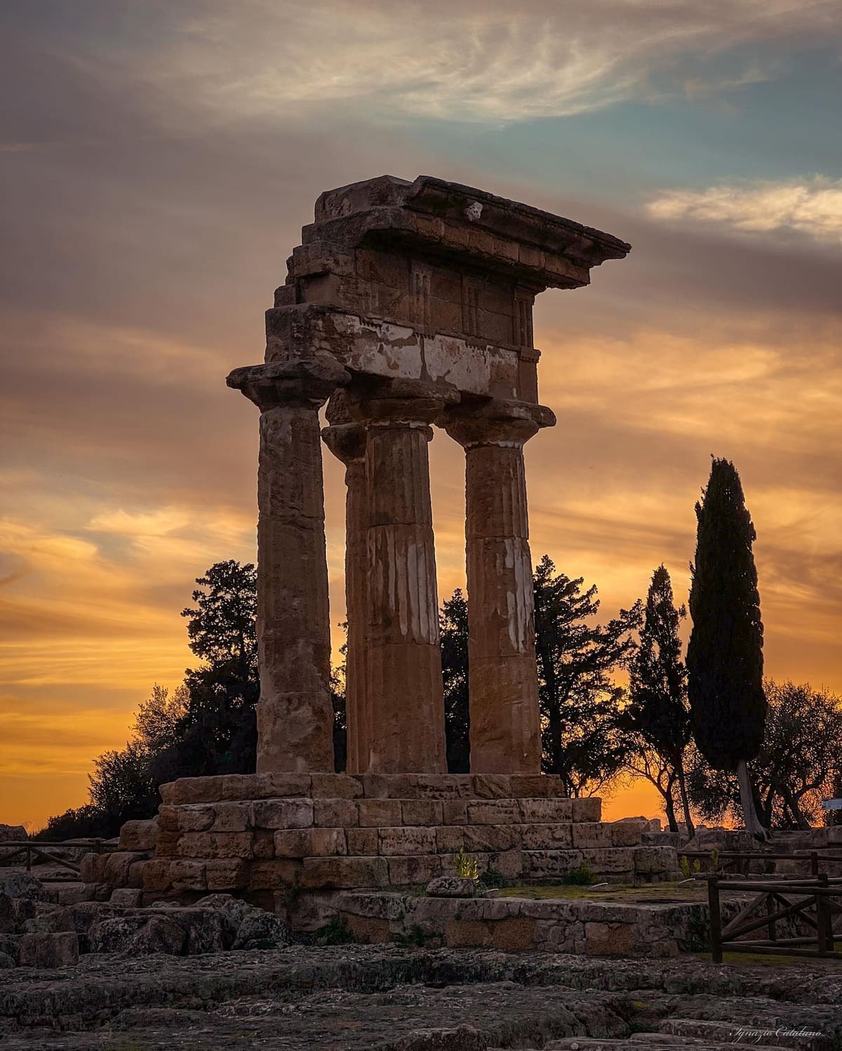 le colonne del tempio dei Dioscuri con il loro pezzo di trabeazione, controluce al tramonto fra i cipressi