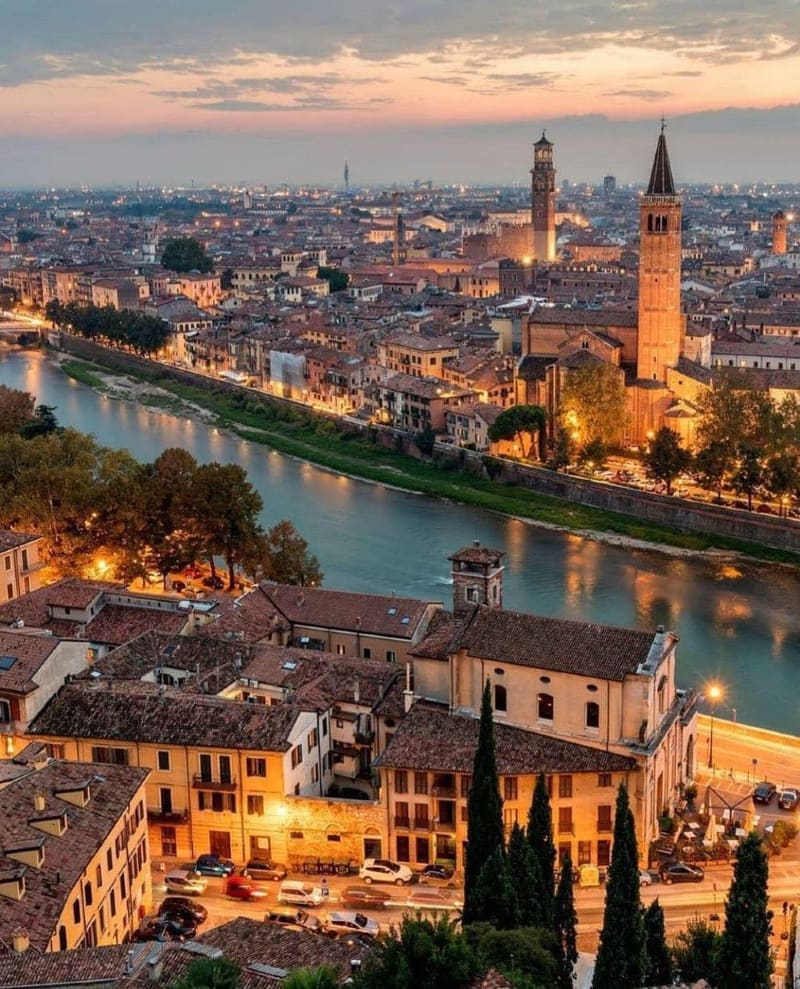 il centro storico e l'ansa dell'Adige al tramonto, con le torri e i campanili sopra i tetti