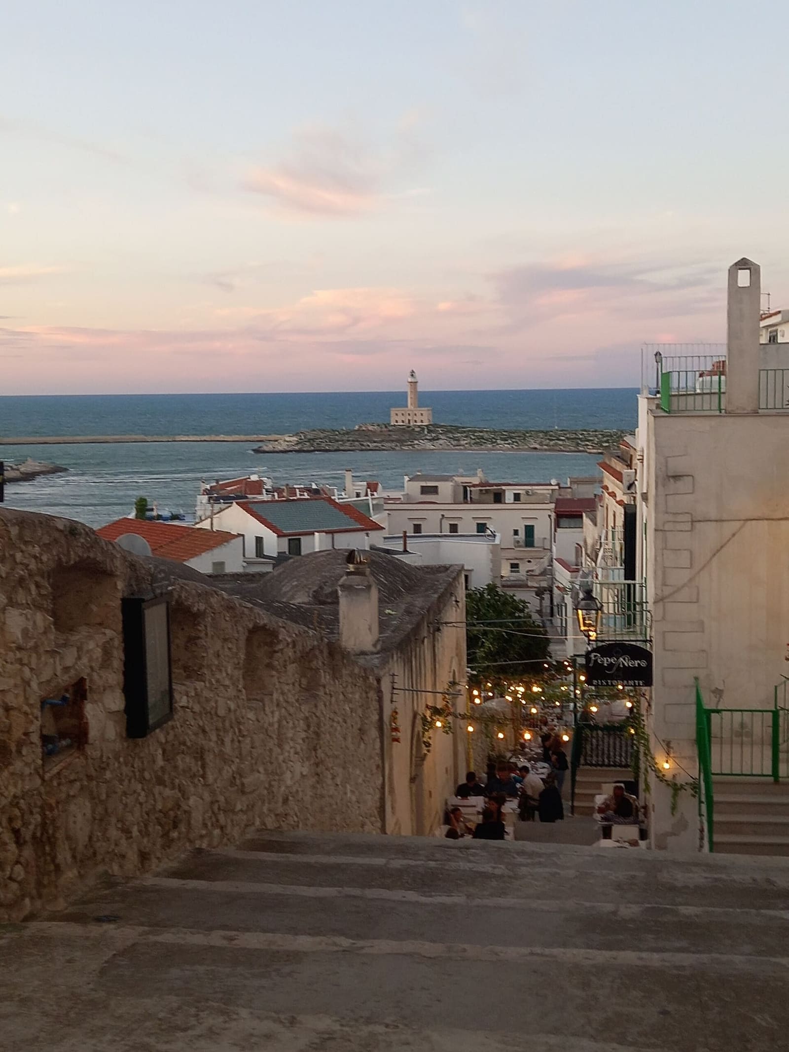 una scalinata del centro storico la sera, con i tavoli dei ristoranti e il faro in fondo